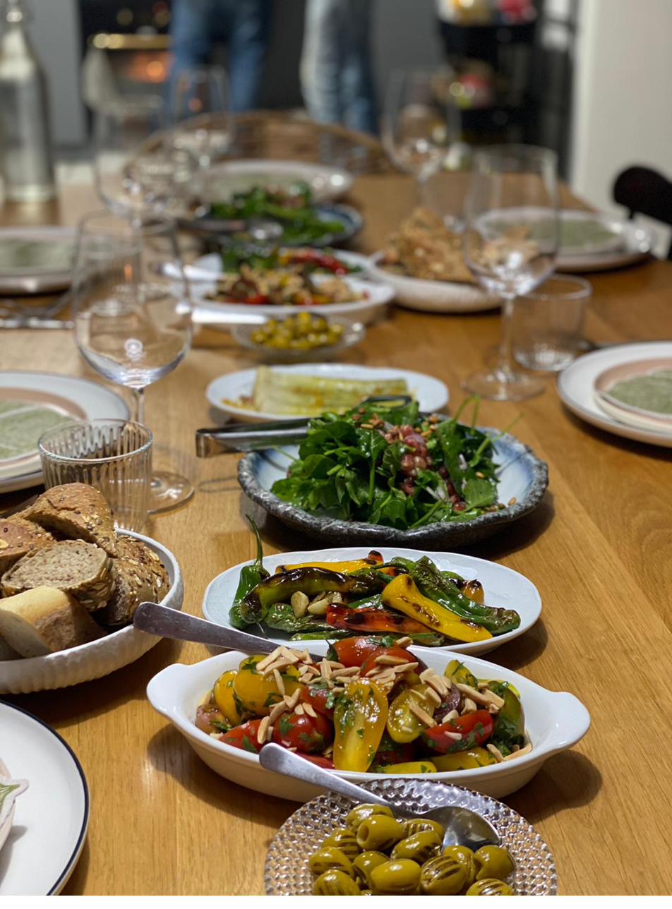 Family-style table with salatim, grilled peppers, and salads